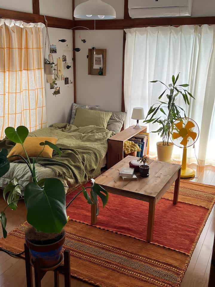 温かみのある木目調とナチュラルグリーンが印象的な一人暮らしの寝室、ベッドとコーヒーテーブル、多数の植物が配された居心地のよい空間