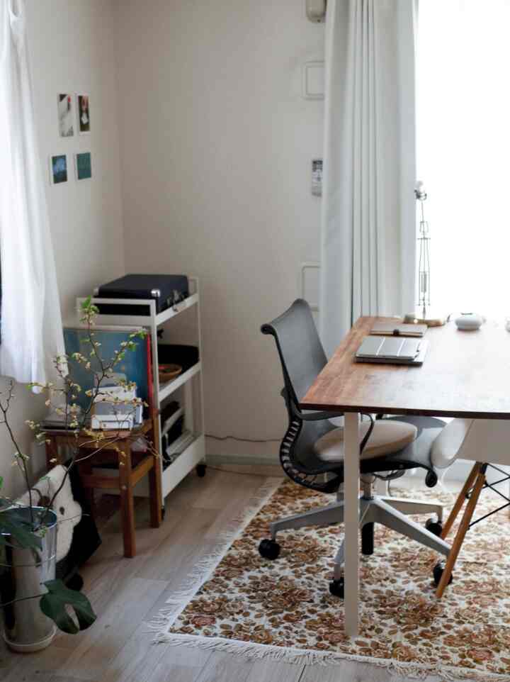 白い壁とカーテン、木目調のデスクとオフィスチェアが配置されたコンパクトなホームオフィス空間