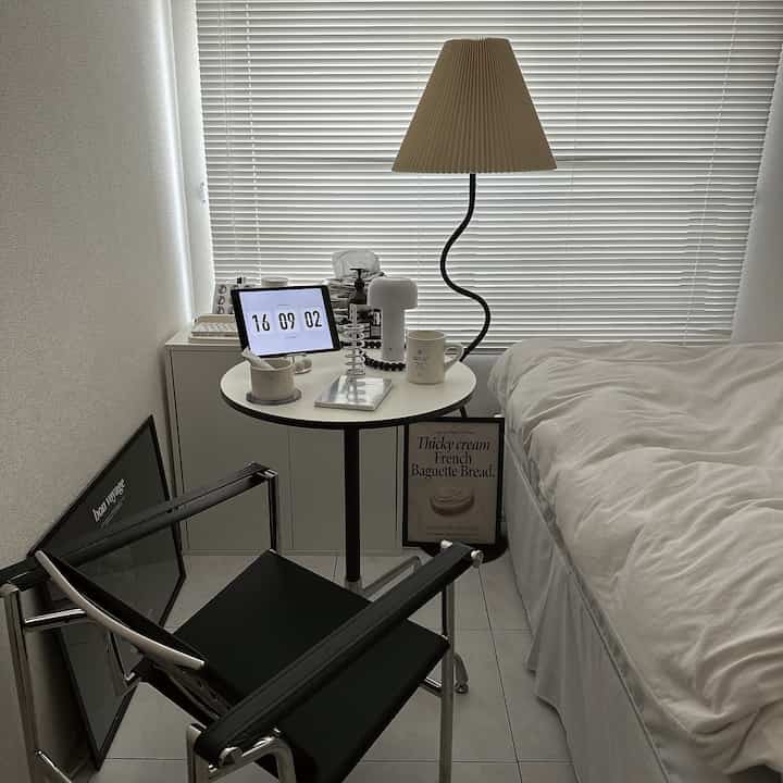 白と黒のトーンの寝室、黒のアームチェアと丸いサイドテーブル、フロアランプが配置されたシンプルモダンな印象的な空間