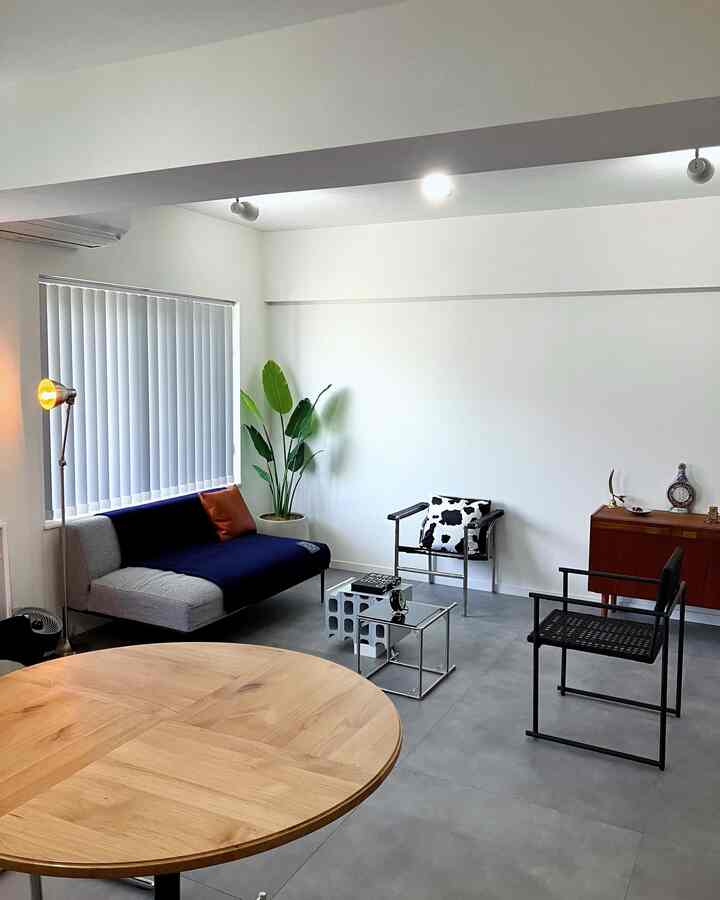 白い壁と木目調のダイニングテーブルが配置されたインダストリアルスタイルのリビング、モダンなソファとフロアランプが整った印象的な空間