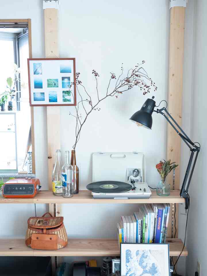 明るい木製の棚と黒いテーブルランプ、本や額縁が配置されたナチュラルでシンプルなリビングルーム