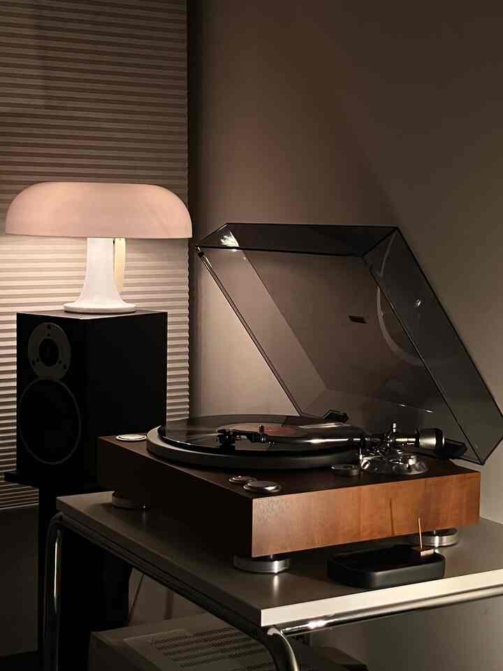 Cozy living room with warm wood tones and beige honeycomb blinds, featuring a table lamp and retro record player