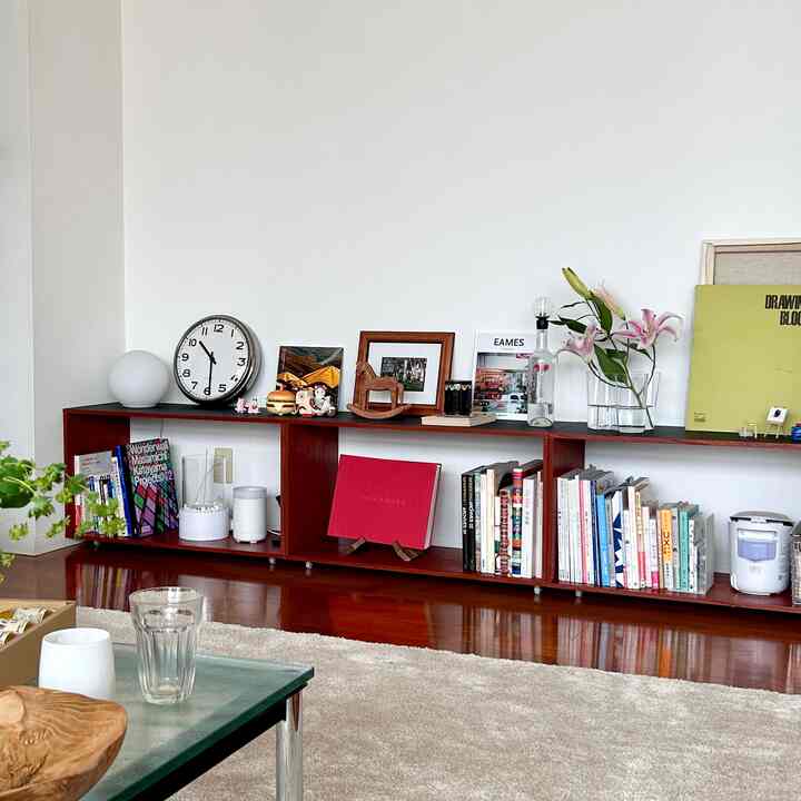 白い壁とダークブラウンの木製棚が配置されたリビング、花瓶や時計などがあるシンプルでナチュラルなインテリア