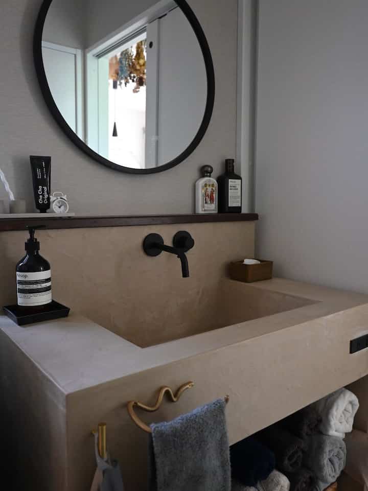 Soft beige modern powder room sink with black round mirror and neatly arranged towels in a minimalistic setting