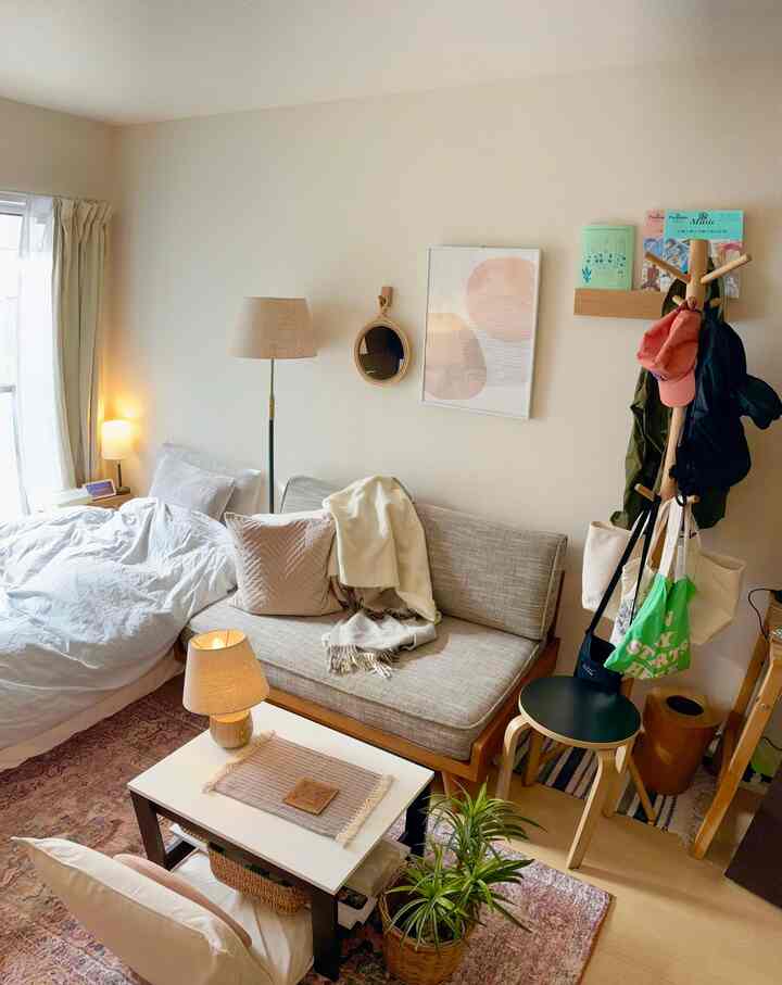 ベージュ系ナチュラルカラーのワンルーム、ソファとベッドが配置された暖かみのある雰囲気のインテリア