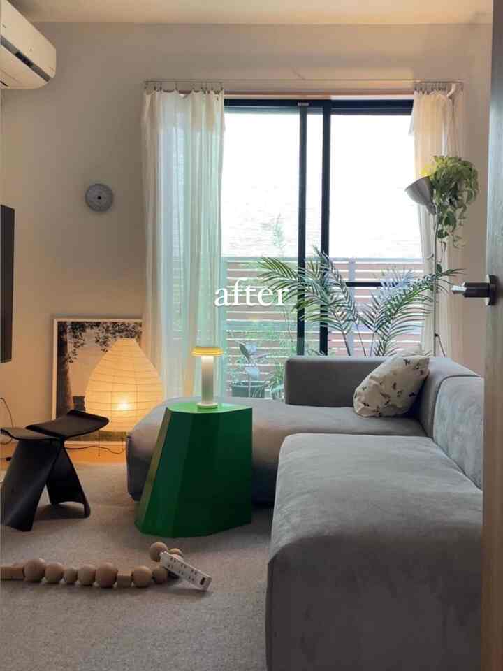 グレーとホワイトの色調のリビング、グレーのセクショナルソファとグリーンスツール、フロアランプと室内植物が配置された落ち着いた雰囲気のインテリア