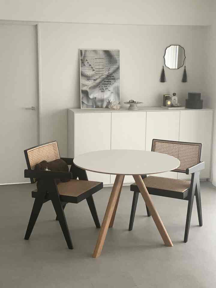 Simple living room with a white round dining table and natural-toned armchairs arranged in a clean, modern style