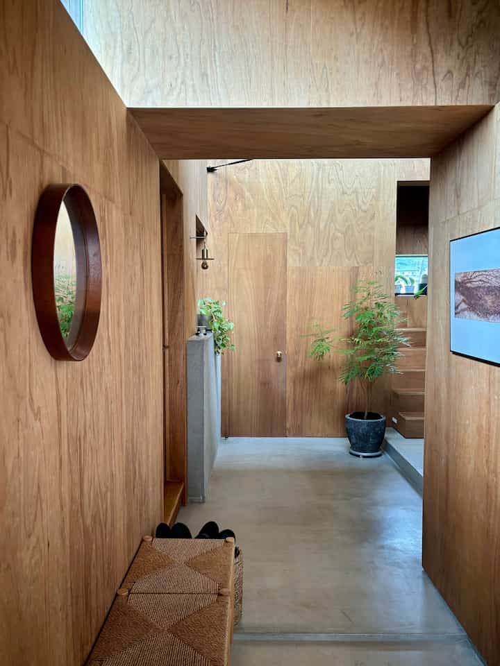 ナチュラルな木目調の壁と天井が印象的な玄関、大きなプランターとベンチが調和した空間