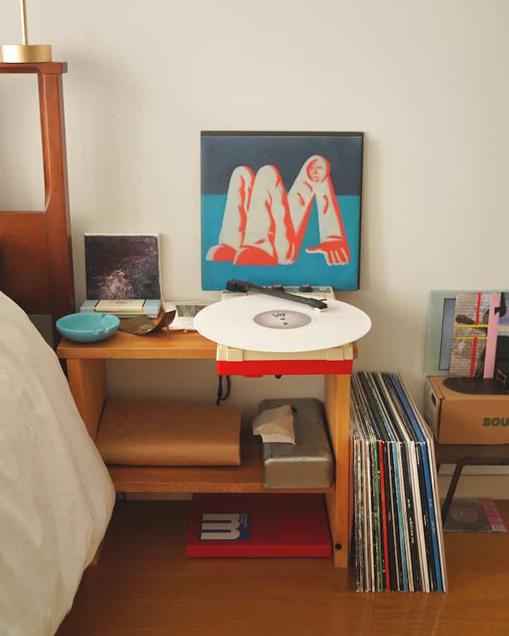 アイボリーの壁と木目調の床の寝室、サイドテーブルにポータブルレコードプレーヤーとレコードが置かれた雰囲気のあるインテリア