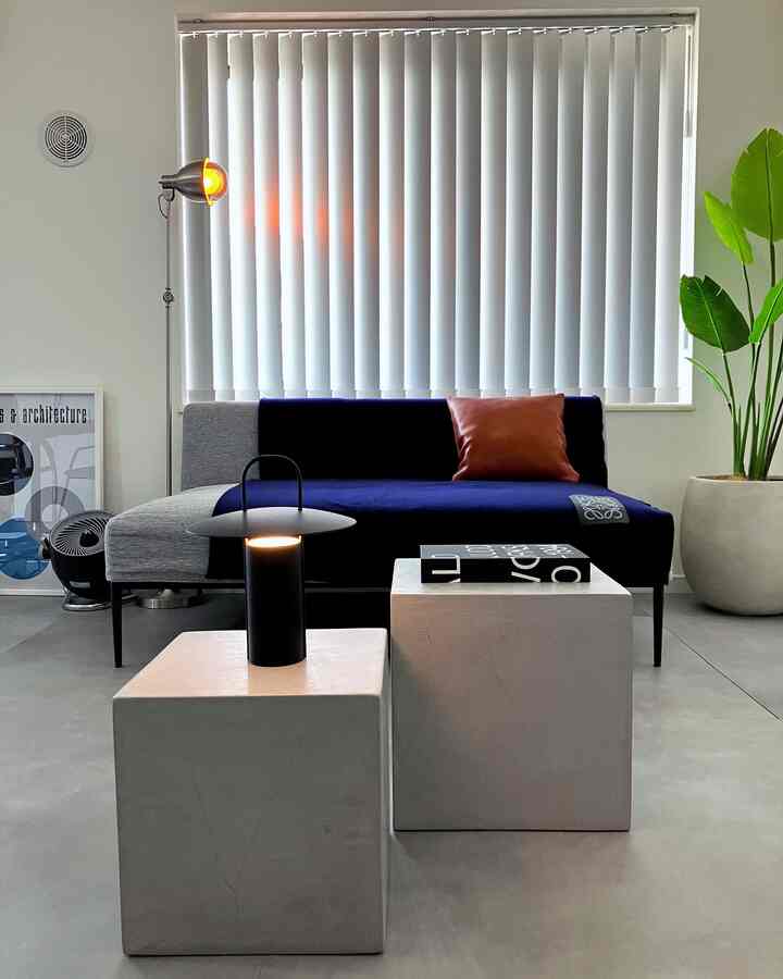 白を基調とした背景にネイビーグレーのソファとシンプルなキューブ形のテーブルが配置された、ミニマルでインダストリアルなリビングルーム