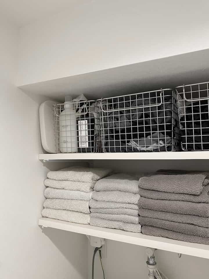 White and gray toned laundry room featuring wire baskets and neatly color-sorted towels, creating a clean and practical space