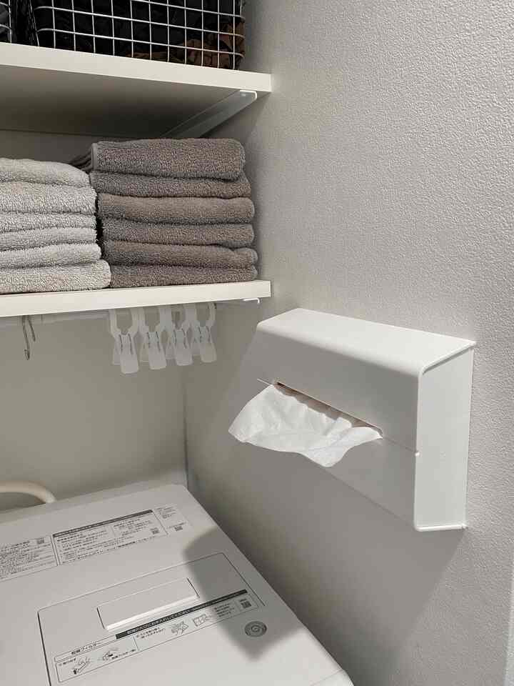 White-toned laundry room featuring neatly stacked towels and a wall-mounted tissue dispenser with a clean, minimalist atmosphere