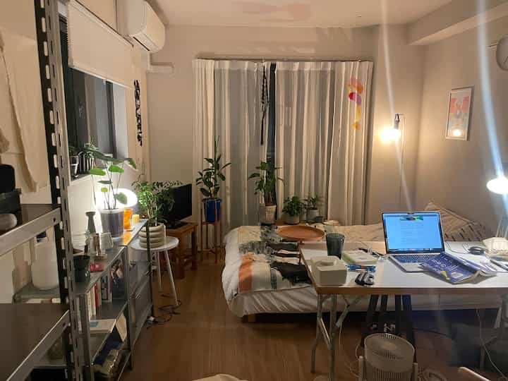 白と木目調が調和した、一人暮らし向けの狭くコンパクトな寝室兼ホームオフィス、植物とデスクが配置された空間