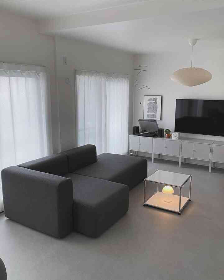 Modern living room in white and gray tones featuring dark gray sofa, side table with lamp, and pendant light creating a clean atmosphere