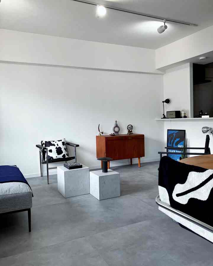 白とグレーのトーンのシンプルなリビング、メタルアームチェアとミッドセンチュリーのキャビネット、コンクリートのキューブテーブルが配置されたモダンな雰囲気のインテリア