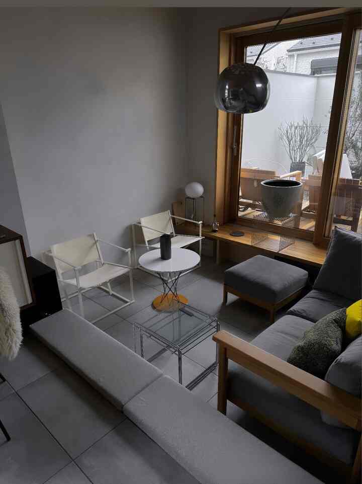 グレーとナチュラルトーンのリビング、モダンなソファとアームチェア、ガラスのコーヒーテーブルが配置されたミニマルな空間