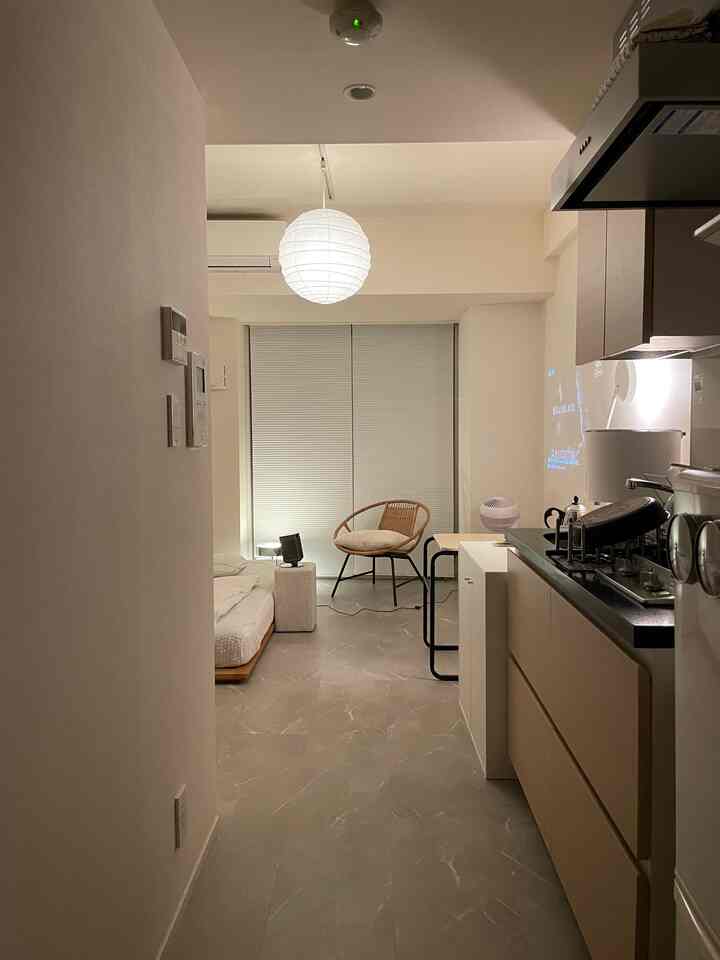 Minimalist studio apartment in white and natural tones featuring a bed, armchair, and integrated kitchen with a calm atmosphere