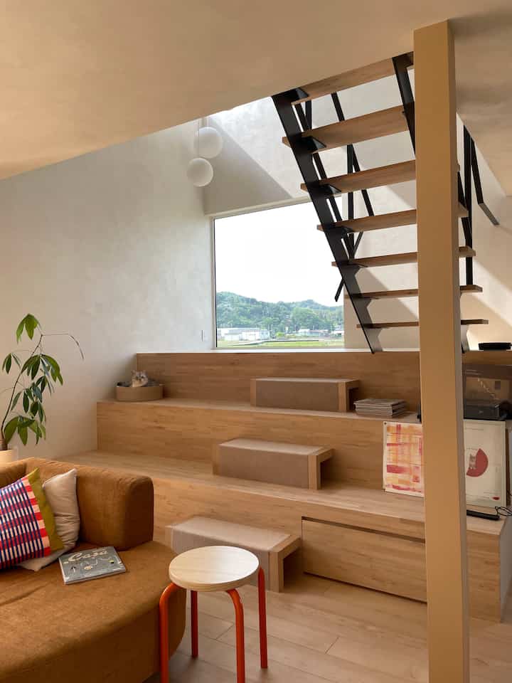 ナチュラルな色調の階段空間、キャットタワーやソファ、スツールが配置された温かみのあるモダンなリビングインテリア