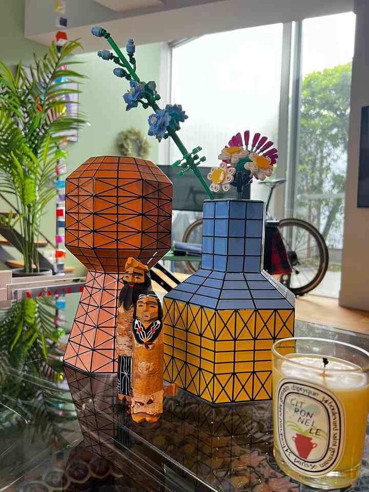 Living room with bright yellow and blue geometric vases, wooden carved accessories on glass table, and natural plants creating a cozy colorful atmosphere