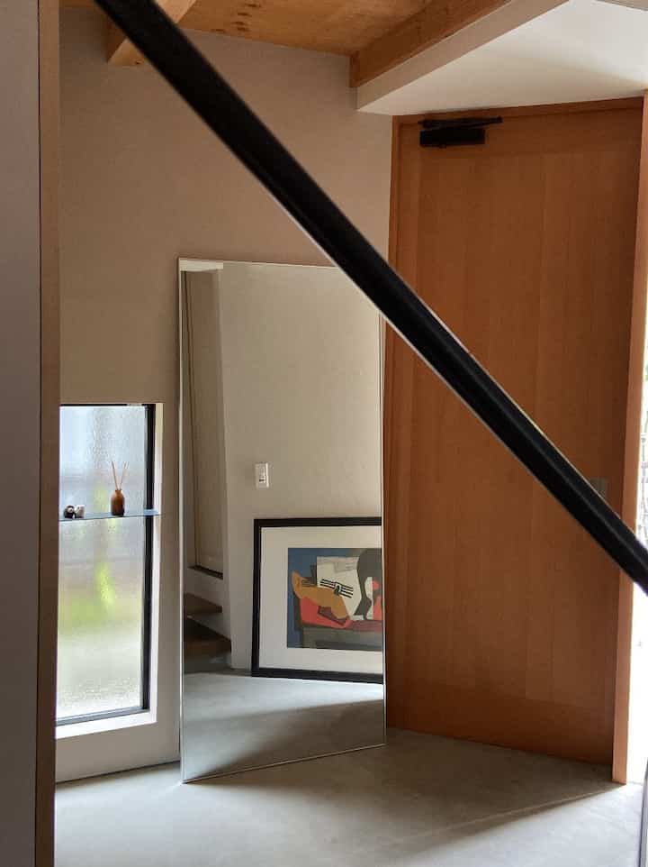 ナチュラルなブラウンの木製ドアとコンクリート床が調和したシンプルでモダンな玄関、鏡とポスターが配置された雰囲気のあるインテリア