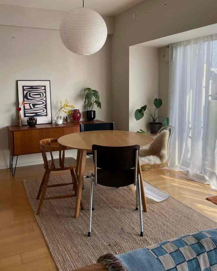 Natural-toned dining room featuring a light brown wooden table and chairs, jute rug, plants, and soft lighting creating a cozy atmosphere