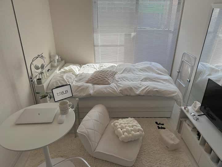 白とナチュラルトーンの6畳1K寝室、ベッド・デスク・椅子・ラグが配置されたシンプルで落ち着いた雰囲気のインテリア