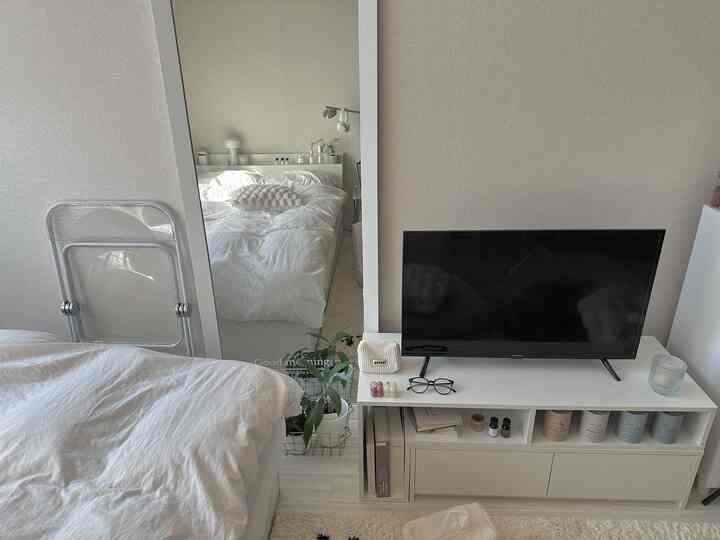 ホワイトとナチュラルトーンの寝室、大きな鏡とテレビ台が配置された清潔感のあるシンプルなインテリア