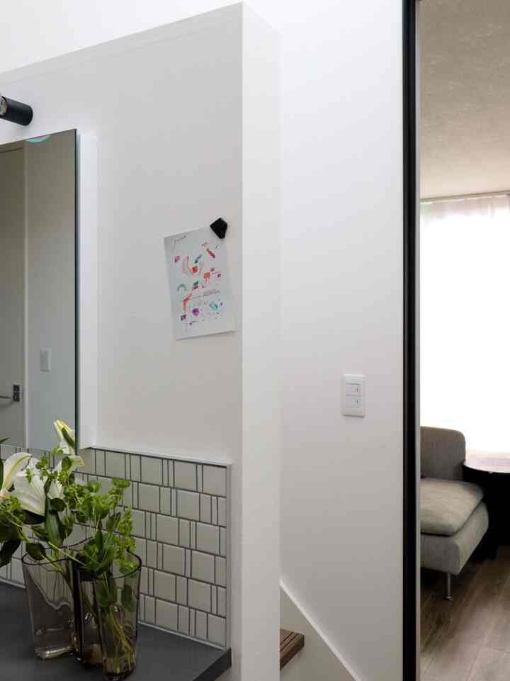 白い壁とタイルのあるバスルーム、洗面台に花瓶と自然なインテリアが配置された明るい空間