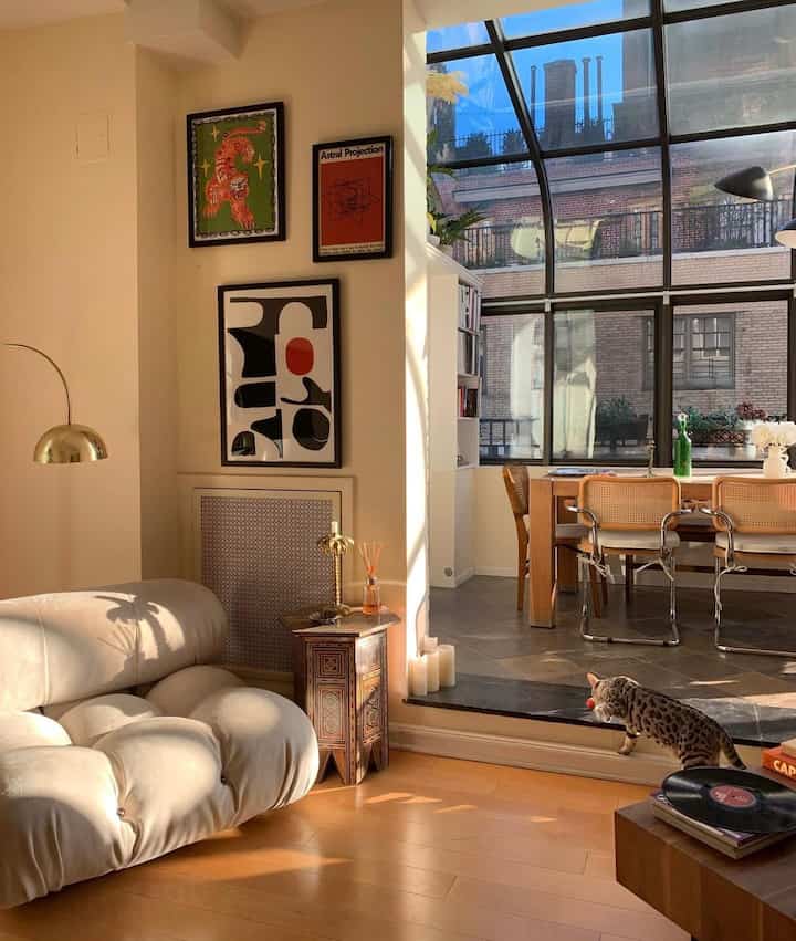 Warm natural-tone living and dining room featuring cream sofa and wooden dining table with a cat walking near the floor
