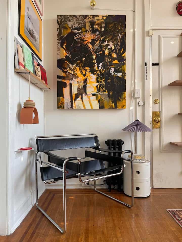 A small living room with white walls and wood-toned floor featuring a modern black armchair and abstract painting creating a cozy atmosphere