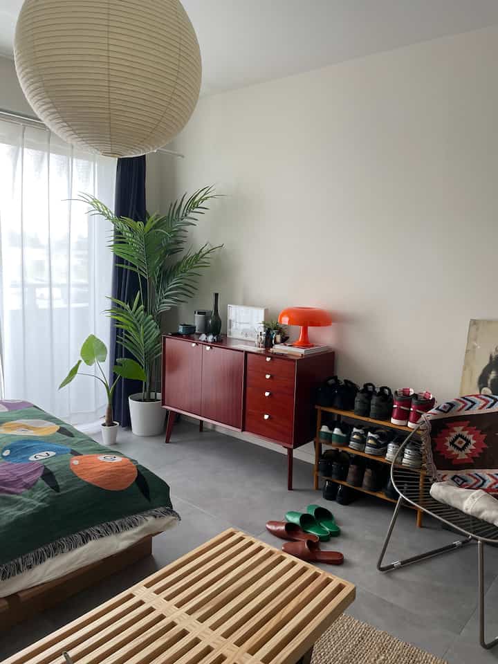 A white and wood-tone living room featuring a colorful sofa bed, wooden sideboard, green plants, and a simple Nordic style atmosphere