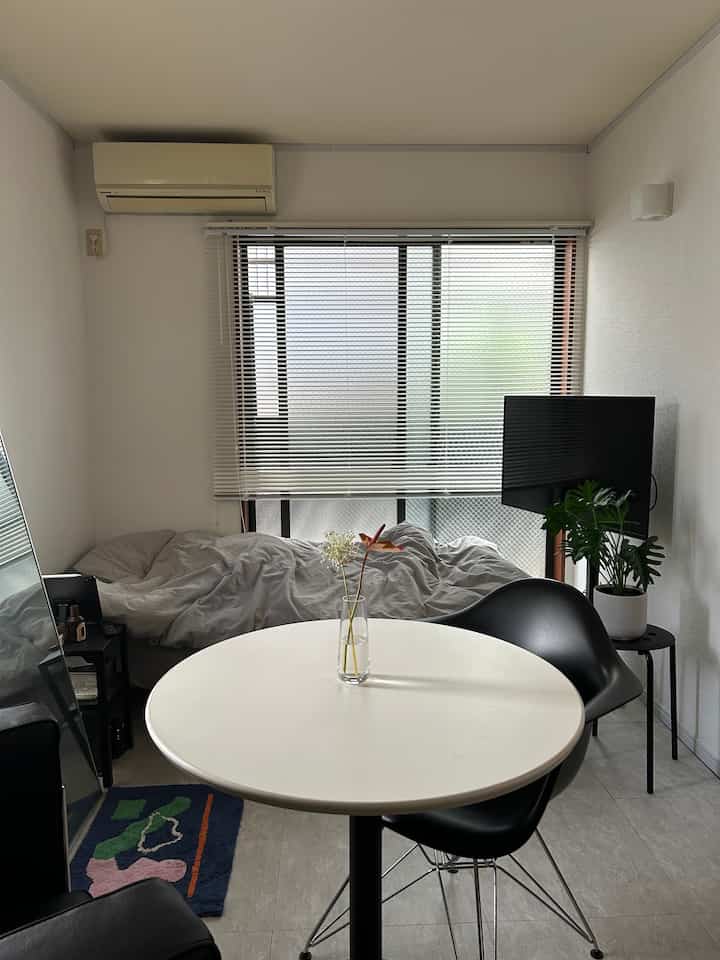 白と黒のトーンでまとめられたワンルームの寝室、丸いダイニングテーブルとデザイナーズチェアが配置されたシンプルモダンな空間