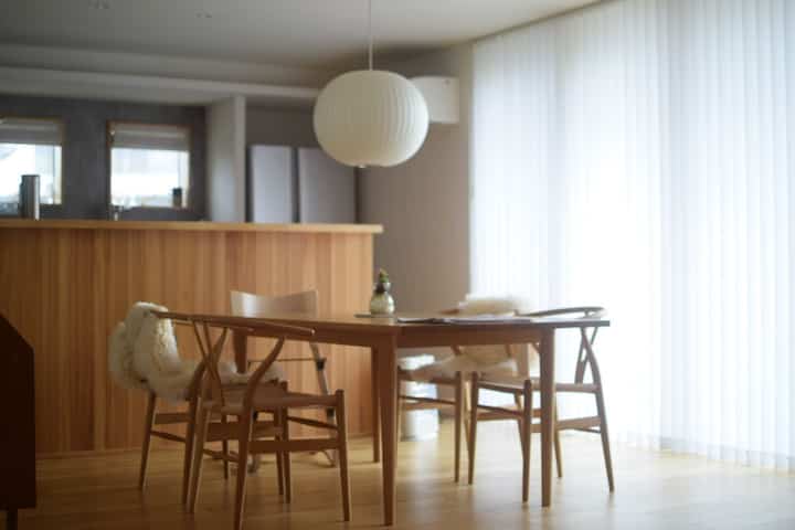 Wood tone and silver harmonize in a simple Japandi style dining room featuring a bubble pendant light and dining table centrally placed