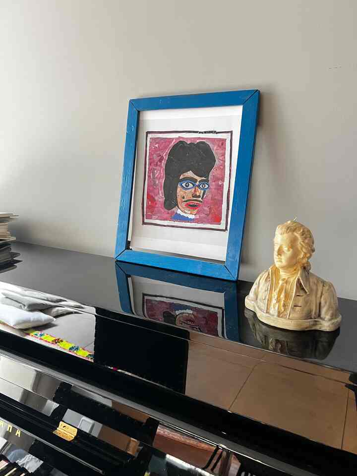 Simple space featuring a black piano with a blue picture frame and decorative objet on top