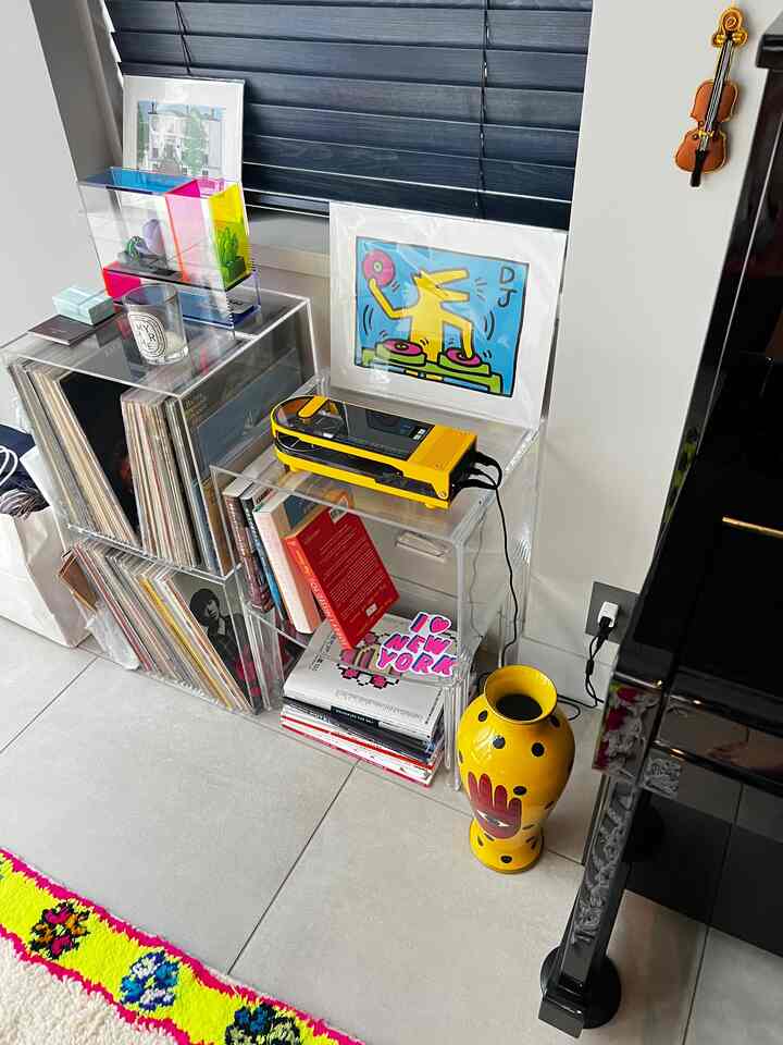 青いブラインドを背景に、透明な棚にレコードや本、黄色いオーディオ機器が置かれたレトロな雰囲気のリビングコーナー