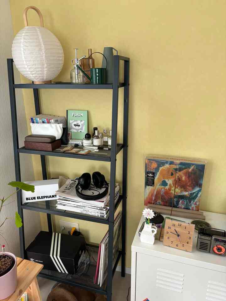 Cozy compact room with yellow walls and a dark metal shelf organized with books and decor items
