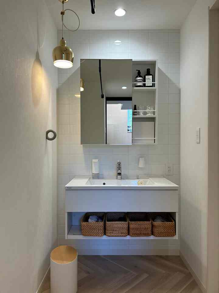 White and wood tone narrow vertical bathroom powder room featuring tidy storage baskets and wall sconce in minimal space