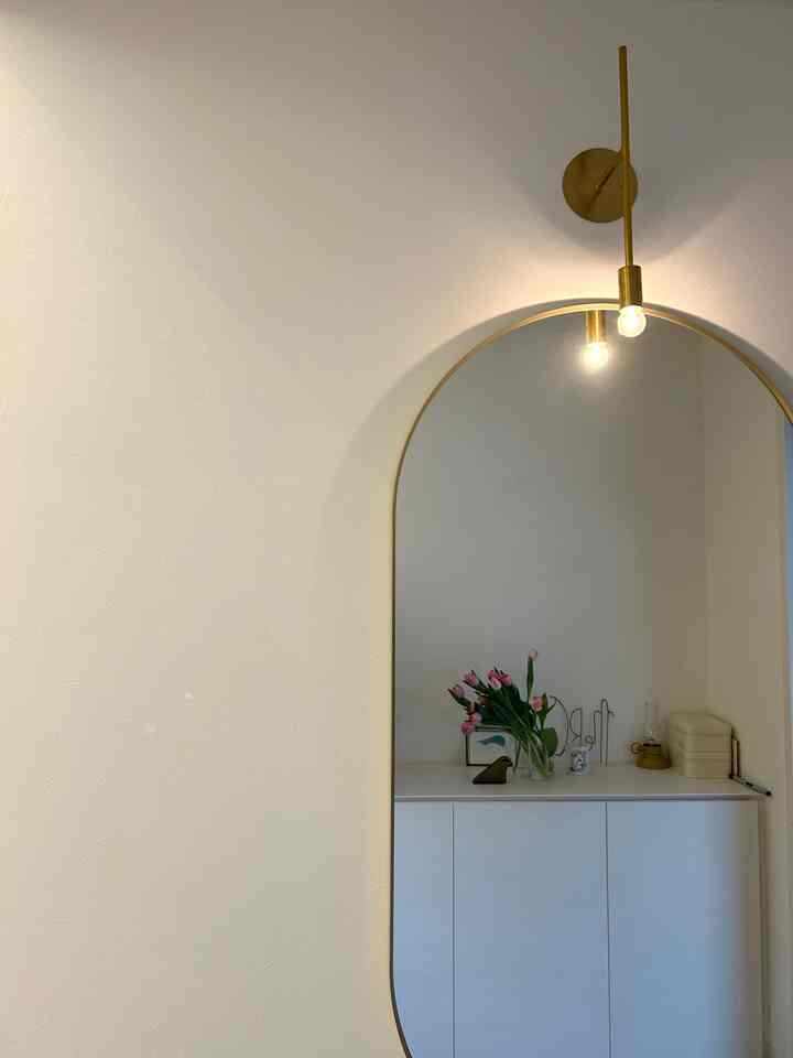 白とゴールドトーンの玄関、丸い鏡と壁掛け照明が柔らかな雰囲気を醸し出すインテリア