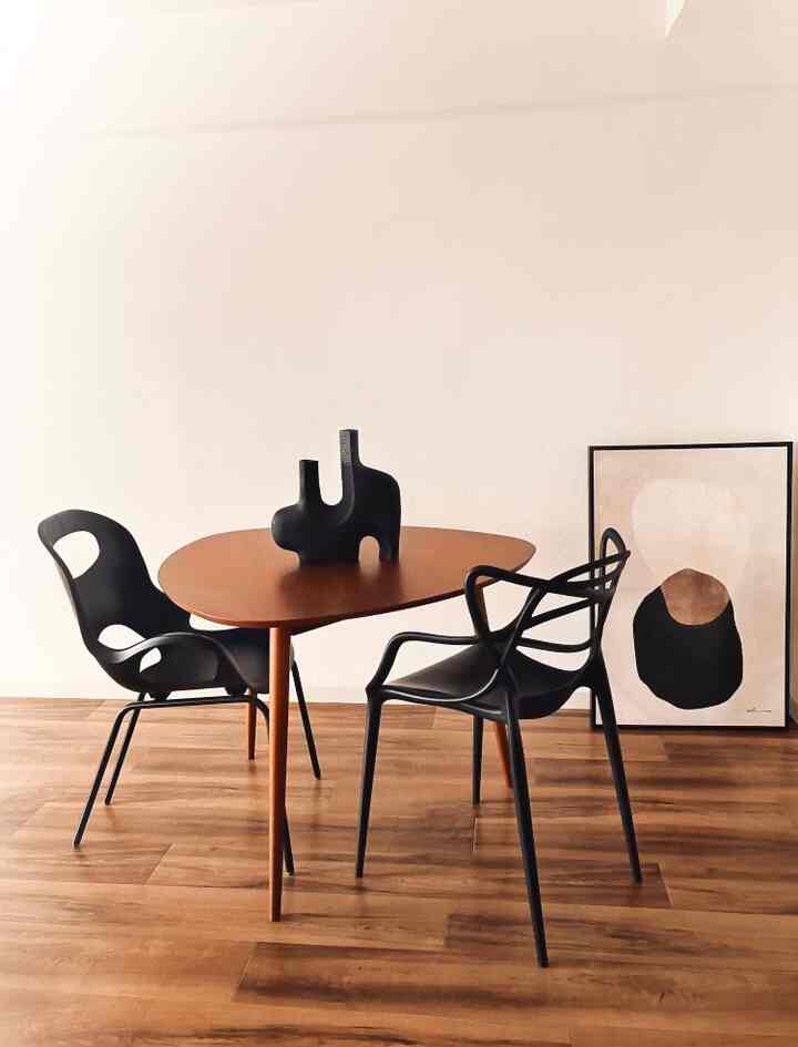 Simple modern dining room with warm wood-tone floor and dining table, featuring black dining chairs and abstract objet centerpiece