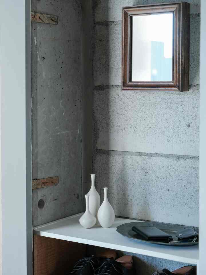 ナチュラルトーンのコンパクトな空間、白い花瓶3点と木枠の鏡が配置されたシンプルな収納棚