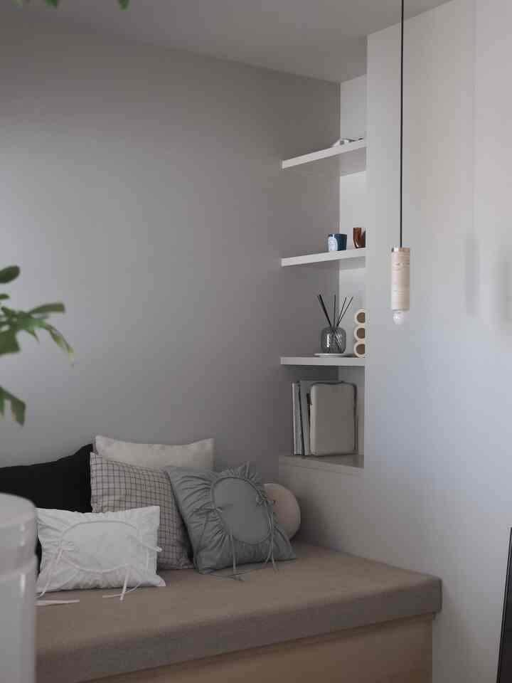White and natural-tone living room corner featuring beige sofa with cushions, a niche shelf with diffuser, and pendant light creating a cozy ambiance