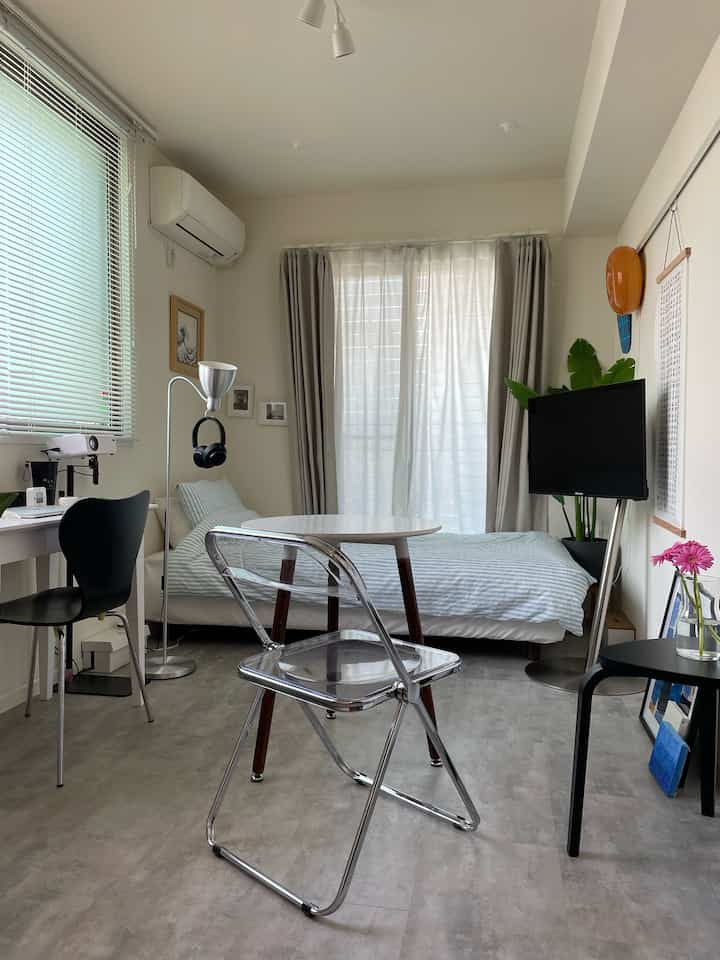 A white and gray toned compact single bedroom featuring a transparent chair, desk, and modern minimalist decor