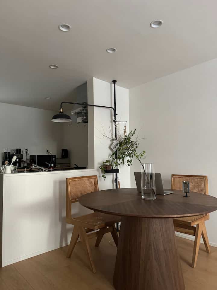 ブラウンとホワイトの色調の2LDKダイニング、丸テーブルと椅子が配置され、キッチンとつながった清潔感と自然な雰囲気のある空間