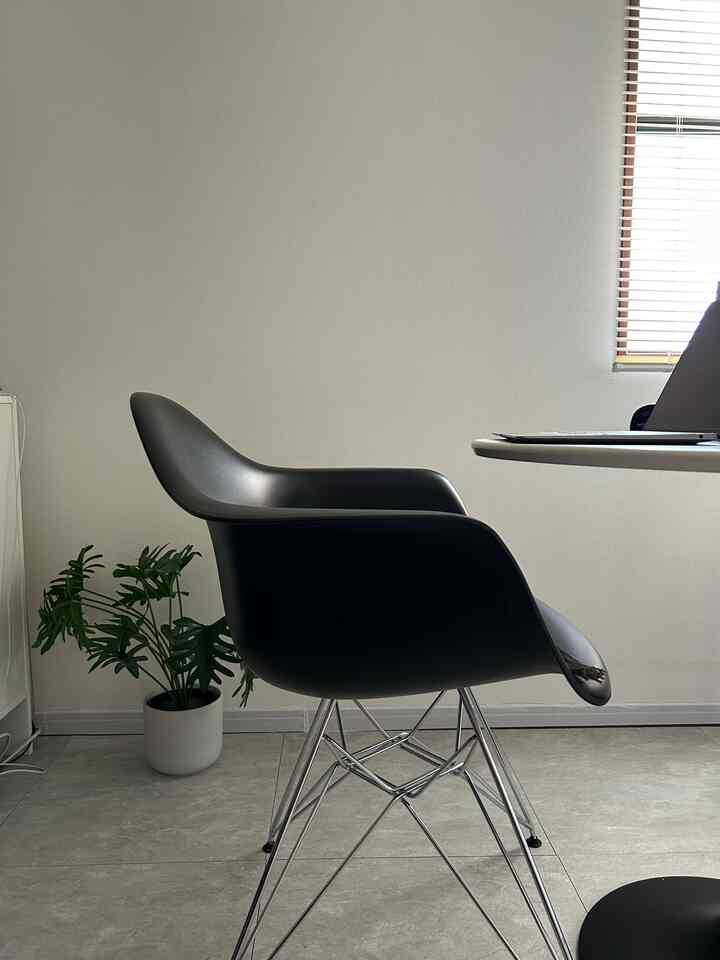 Modern compact home office with white and gray tones, featuring a black Eames-style armchair and a green plant