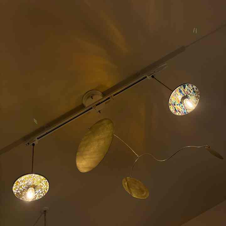 金色のモビールと多彩なガラス製ペンダントライトがある暖かい色調の天井照明インテリア
