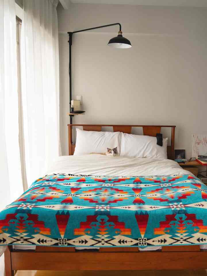 ホワイトとウッドトーンの調和がとれた寝室、中央に鮮やかな柄のスローと猫がいる温かみのある空間