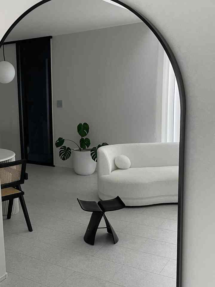 白と黒の調和が印象的なリビング、曲線のソファと黒のスツール、観葉植物が配置されたモダンで清潔感のあるインテリア