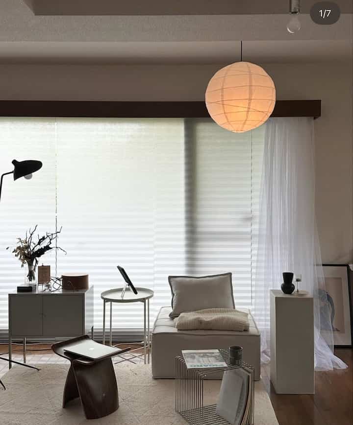 白とナチュラルな色調のリビング、シンプルなソファとサイドテーブル、丸いペンダントライトが配置された雰囲気のある空間