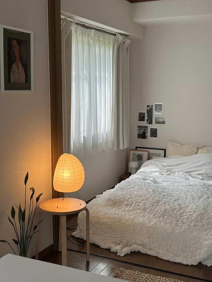 Natural color and wood tone single household bedroom with simple furniture, soft lighting from floor lamp, and clean duvet cover