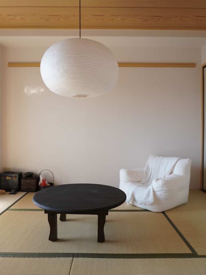 Natural color toned 6-tatami mat room featuring white tofu sofa, black round table, and rice paper pendant light in Wa-Modern style